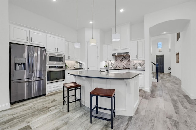 kitchen with white cabinetry, under cabinet range hood, arched walkways, and appliances with stainless steel finishes