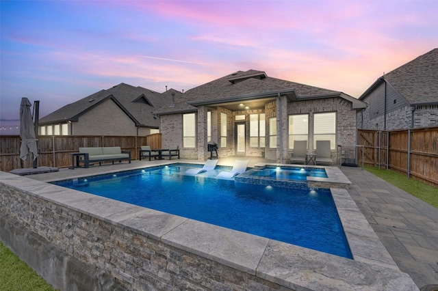 pool at dusk featuring a patio area, a pool with connected hot tub, outdoor lounge area, and a fenced backyard