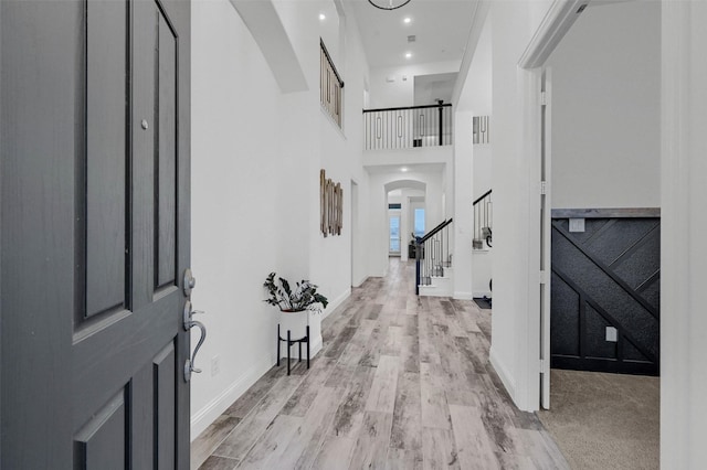 entryway featuring recessed lighting, arched walkways, light wood-style floors, baseboards, and stairs