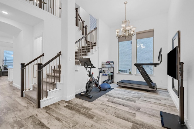 exercise room with a high ceiling, a notable chandelier, wood finished floors, and baseboards