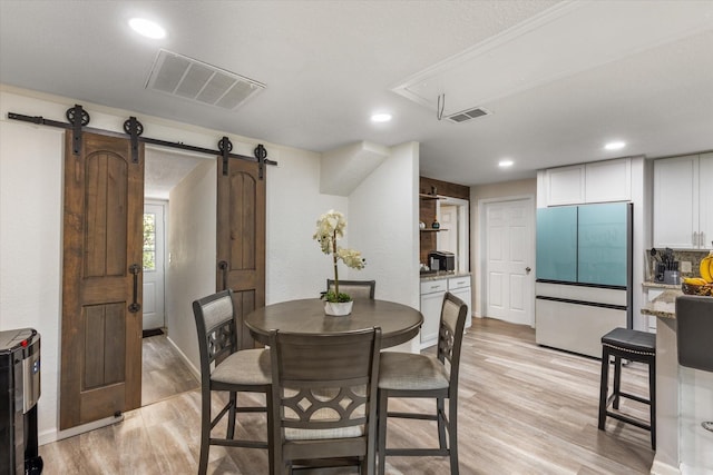 dining room featuring attic access, visible vents, light wood finished floors, and a barn door