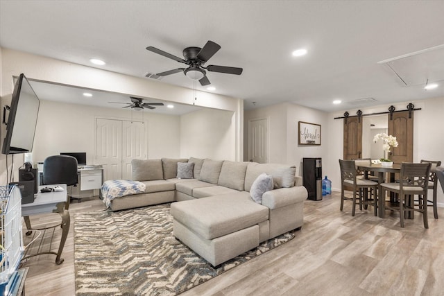 living area featuring attic access, light wood-type flooring, visible vents, and a barn door