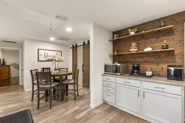 interior space featuring a barn door, light wood-style flooring, visible vents, open shelves, and stainless steel microwave