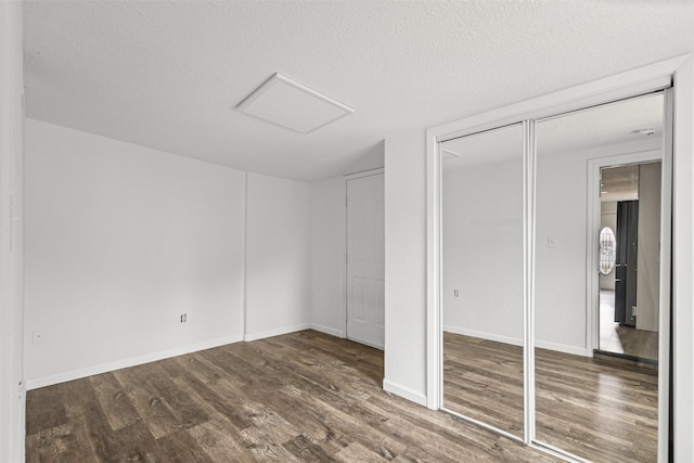 unfurnished bedroom with attic access, a textured ceiling, baseboards, and wood finished floors