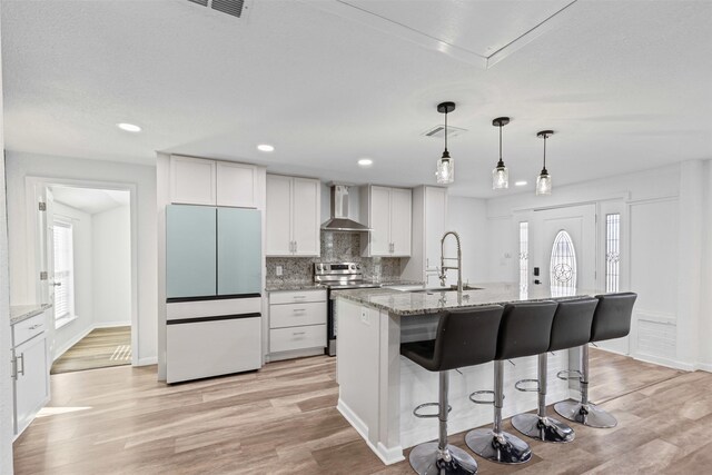 kitchen featuring stainless steel appliances, visible vents, wall chimney range hood, light wood-type flooring, and decorative backsplash