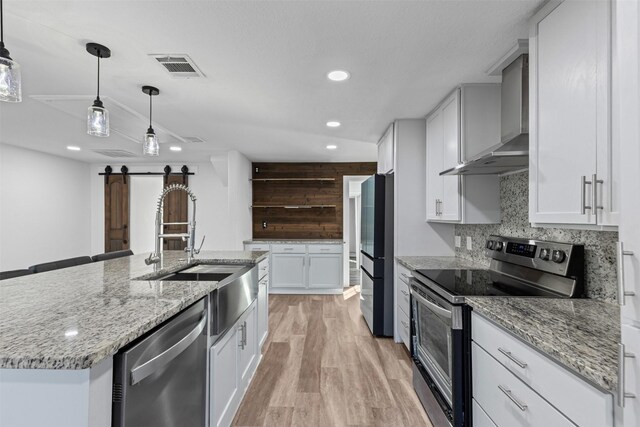 kitchen featuring tasteful backsplash, visible vents, appliances with stainless steel finishes, wall chimney range hood, and a sink