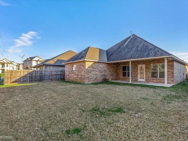 rear view of property with brick siding, a patio, a lawn, and fence