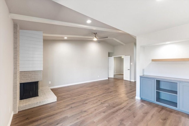 unfurnished living room with lofted ceiling with beams, ceiling fan, a brick fireplace, and wood finished floors