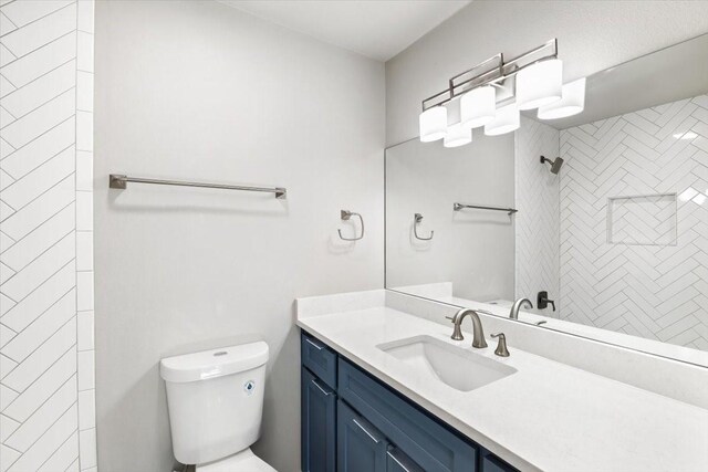 bathroom with tiled shower, vanity, and toilet