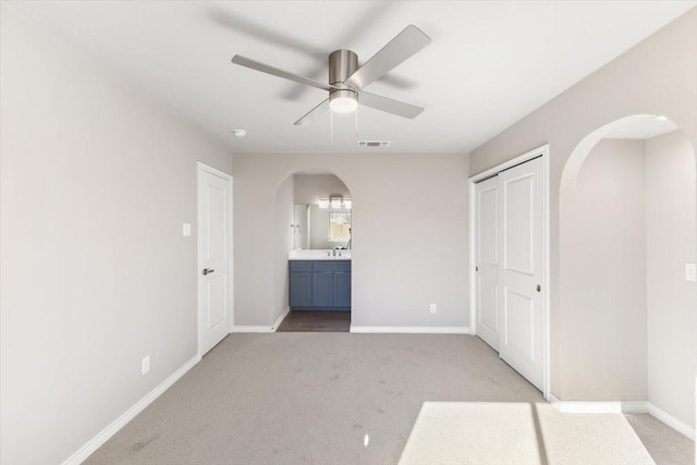 unfurnished bedroom with light colored carpet, arched walkways, visible vents, and baseboards