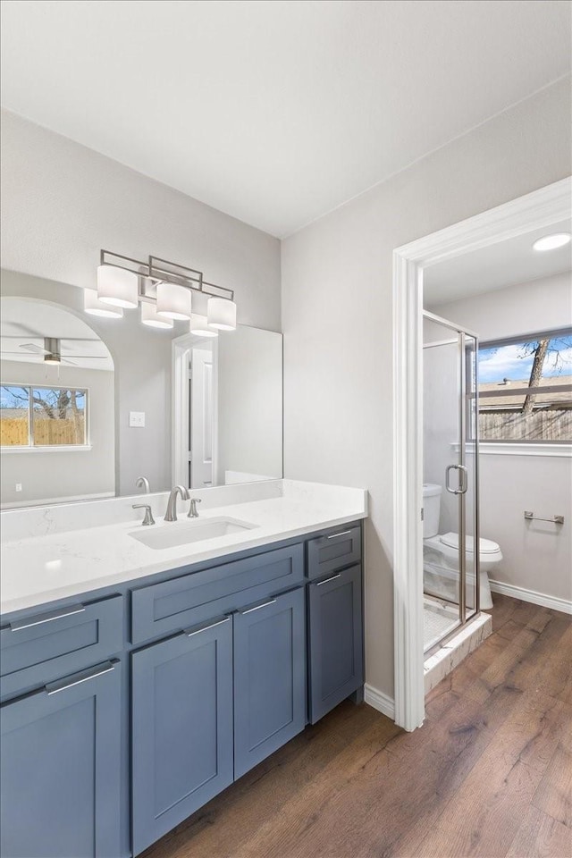 full bath with toilet, a stall shower, vanity, wood finished floors, and baseboards