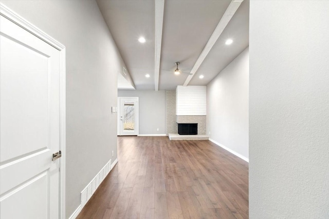 unfurnished living room with baseboards, visible vents, wood finished floors, beamed ceiling, and a fireplace