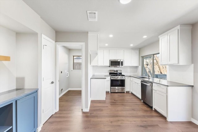 kitchen with stainless steel appliances, visible vents, white cabinets, a sink, and wood finished floors