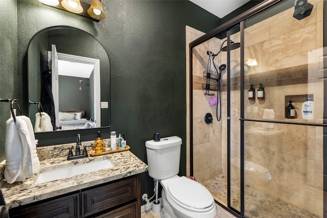 ensuite bathroom featuring ensuite bathroom, a textured wall, toilet, vanity, and a stall shower