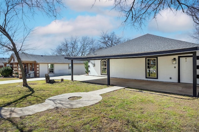 rear view of house with roof with shingles, a yard, a patio, and stucco siding