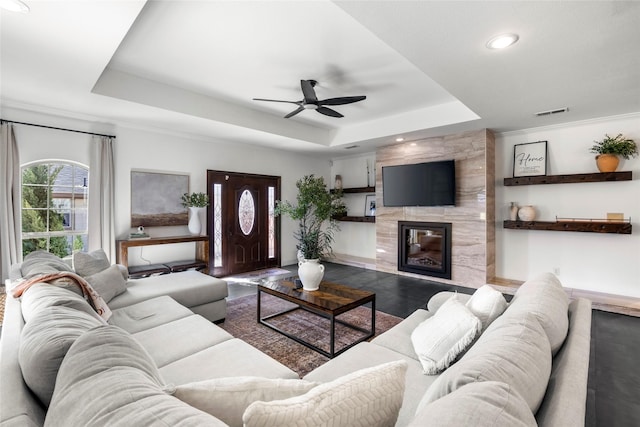 living area with a raised ceiling, visible vents, a premium fireplace, ceiling fan, and wood finished floors