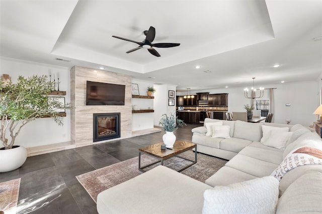 living area with visible vents, a tray ceiling, ceiling fan with notable chandelier, and a high end fireplace