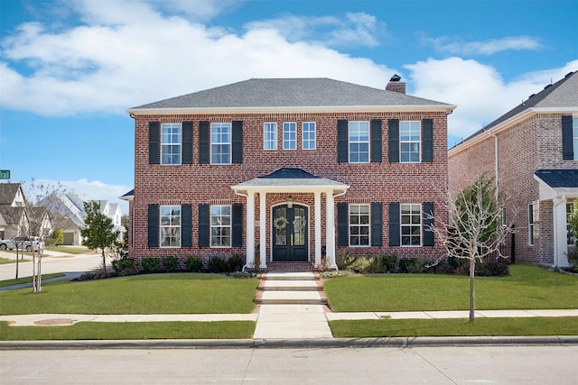 view of front of house featuring brick siding, roof with shingles, a chimney, and a front yard