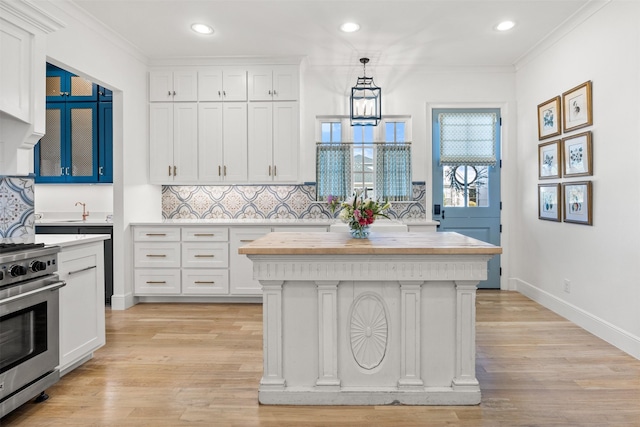 kitchen featuring high end stove, light wood finished floors, white cabinets, and crown molding