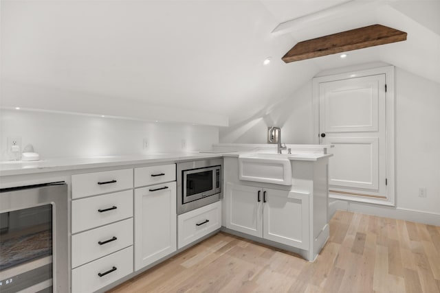 kitchen featuring beverage cooler, lofted ceiling, stainless steel microwave, light wood-style floors, and white cabinetry