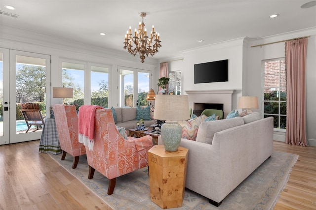 living room featuring a fireplace, visible vents, light wood-style floors, ornamental molding, and french doors