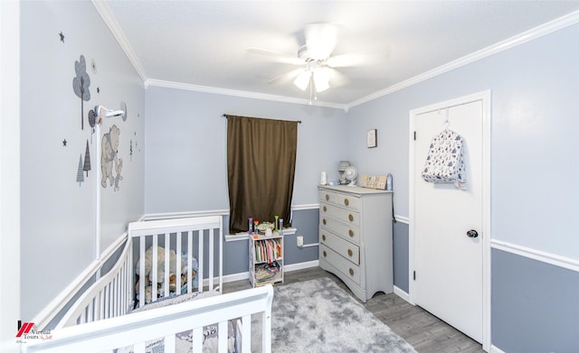 bedroom featuring ceiling fan, baseboards, light wood-type flooring, a crib, and crown molding