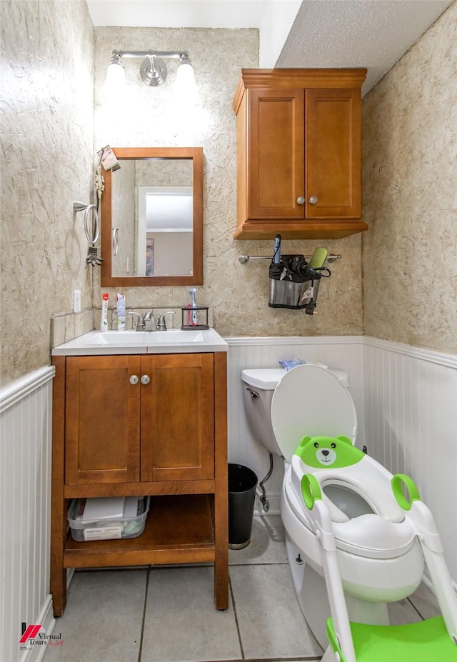 half bath featuring tile patterned flooring, a wainscoted wall, vanity, and toilet