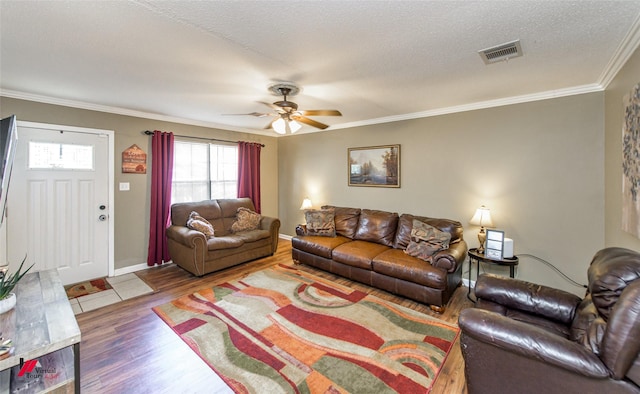 living room featuring a textured ceiling, wood finished floors, visible vents, a ceiling fan, and ornamental molding