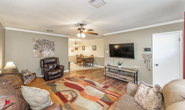 living room featuring a textured ceiling, ornamental molding, wood finished floors, and visible vents