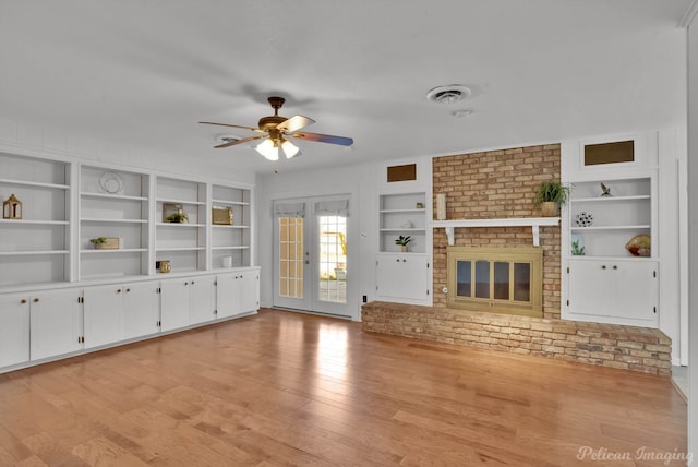 unfurnished living room featuring built in shelves, a ceiling fan, visible vents, a brick fireplace, and light wood-type flooring