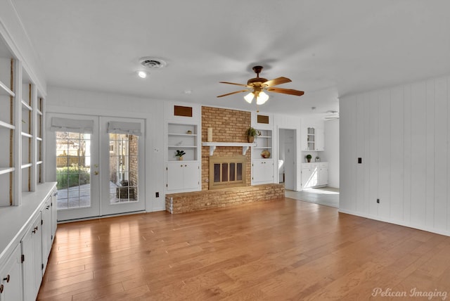 unfurnished living room with built in features, a fireplace, ceiling fan, hardwood / wood-style flooring, and french doors