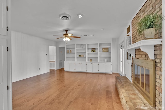 unfurnished living room featuring visible vents, light wood-style flooring, built in features, a brick fireplace, and ceiling fan