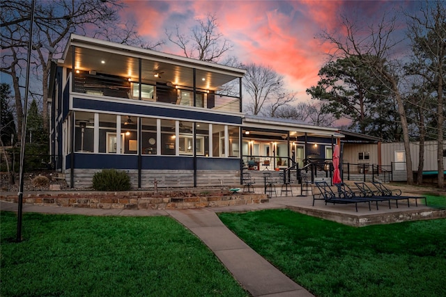 back of property at dusk with a lawn, a patio, a sunroom, a balcony, and ceiling fan