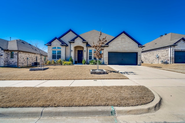 french country home with driveway, stone siding, a garage, and central AC unit