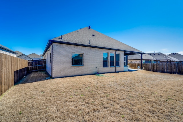 back of property with a fenced backyard, a shingled roof, a lawn, and brick siding