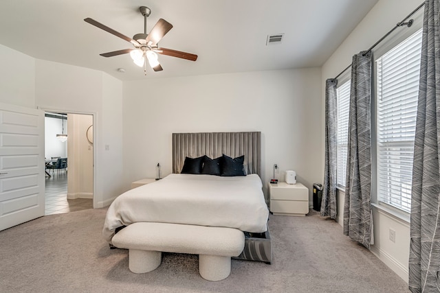 carpeted bedroom with baseboards, multiple windows, visible vents, and a ceiling fan