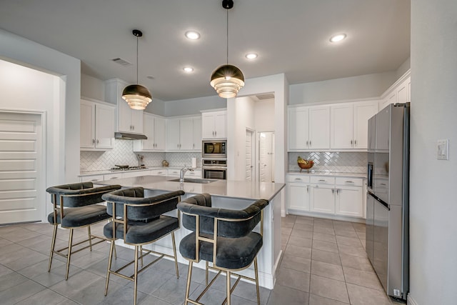 kitchen featuring stainless steel appliances, light tile patterned flooring, a kitchen island with sink, and white cabinetry