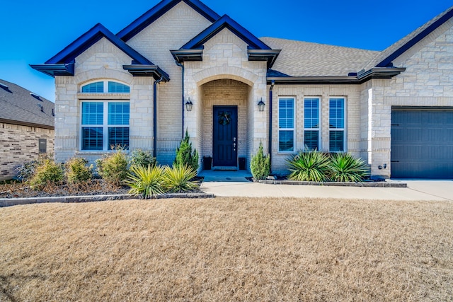 french country inspired facade with stone siding, brick siding, an attached garage, and a shingled roof