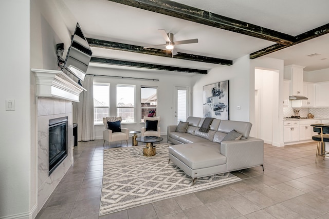 living area featuring light tile patterned flooring, a fireplace, a ceiling fan, baseboards, and beamed ceiling