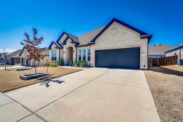 french country inspired facade featuring central air condition unit, a garage, brick siding, fence, and driveway