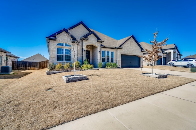 french country inspired facade featuring concrete driveway, fence, a garage, cooling unit, and stone siding