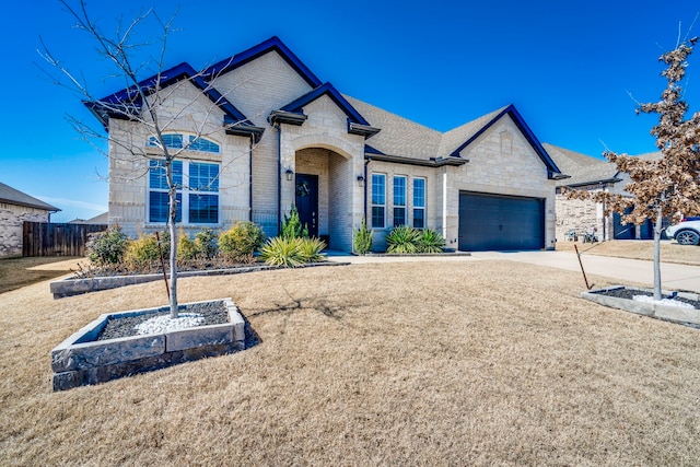 french provincial home featuring an attached garage, brick siding, fence, driveway, and stone siding