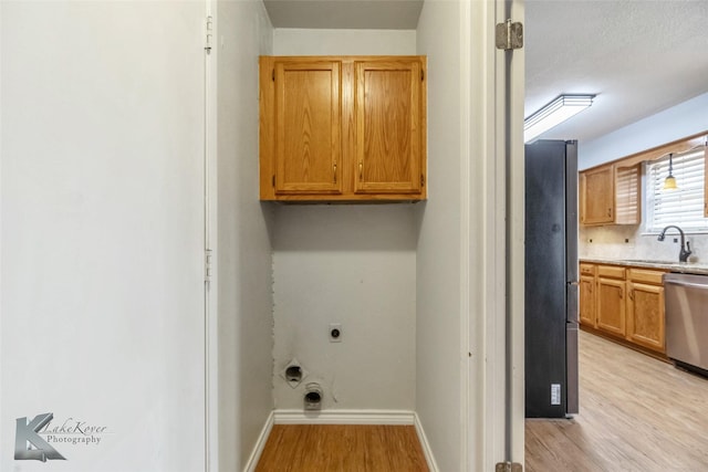 laundry room featuring cabinet space, light wood-style floors, a sink, electric dryer hookup, and baseboards