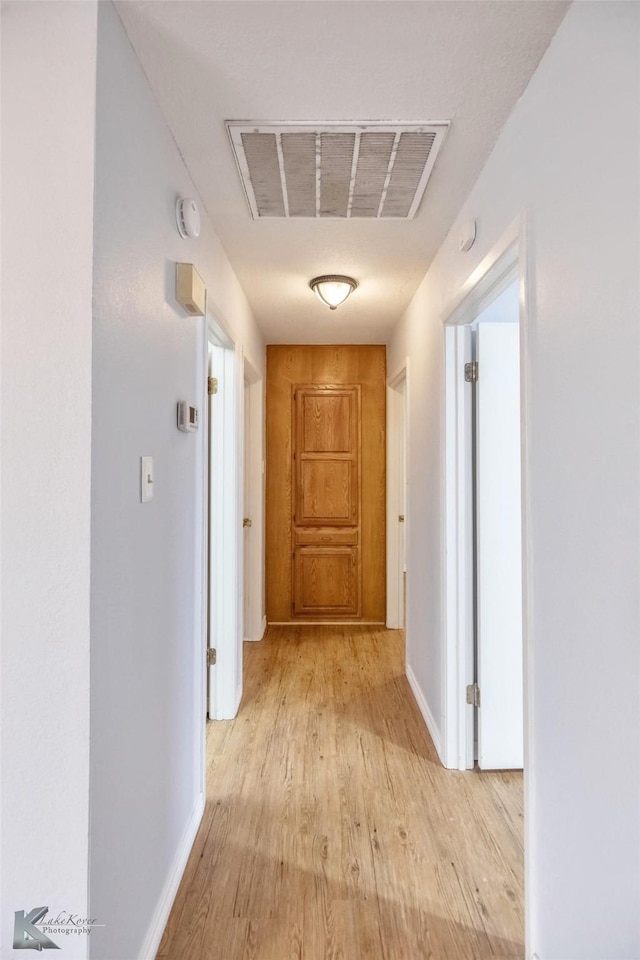 corridor with baseboards, visible vents, and light wood finished floors