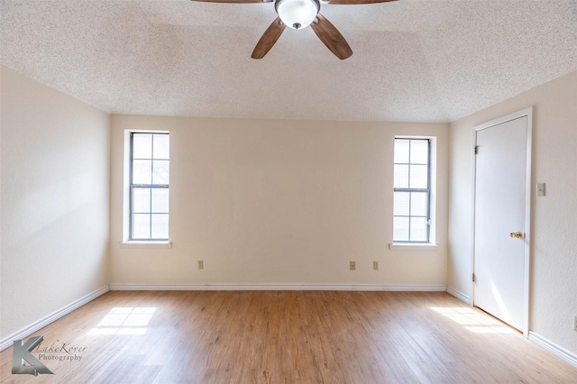 empty room with a textured ceiling, light wood finished floors, a ceiling fan, and baseboards