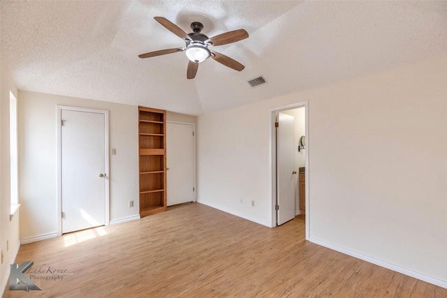 unfurnished bedroom featuring light wood finished floors, baseboards, visible vents, vaulted ceiling, and a textured ceiling