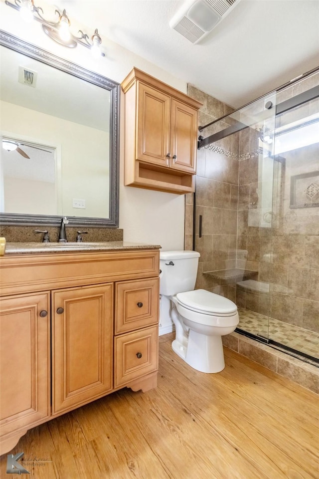 bathroom with toilet, a stall shower, visible vents, and wood finished floors