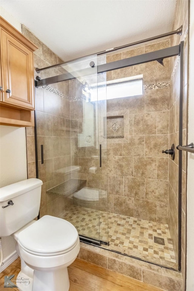 bathroom with wood finished floors, a shower stall, and toilet