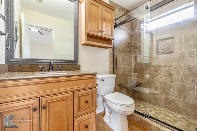 bathroom featuring a stall shower, toilet, ceiling fan, wood finished floors, and vanity