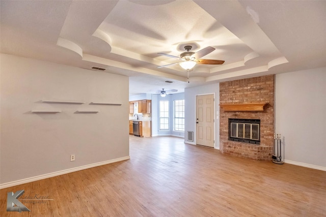 unfurnished living room with a fireplace, a raised ceiling, visible vents, light wood-style floors, and baseboards